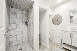 Een badkamer met marmeren tegels, een douche, een wastafel met spiegel en een decoratief wandobject.