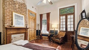 Una habitación con una cama, chimenea, espejo y ventana con cortinas.