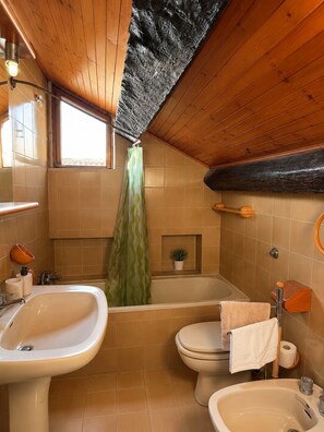 Un baño con bañera, dos lavamanos, inodoro, cortina de ducha y una pequeña planta en maceta.