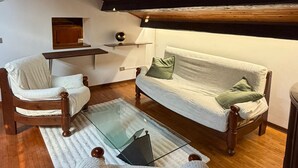 Een gezellig loft slaapkamer met een hoge plafond, houten balken, een dakraam, een bank, een stoel, een tafeltje en een bed.