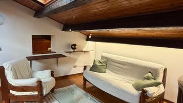 Une chambre à coucher confortable, aménagée dans un grenier avec de hauts plafonds, des poutres en bois, une lucarne, un canapé, un fauteuil, une petite table et un lit.