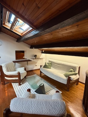 A cozy loft bedroom with a high ceiling, wooden beams, a skylight, a sofa, a chair, a small table, and a bed. - The Old Town Attic (Senigallia)