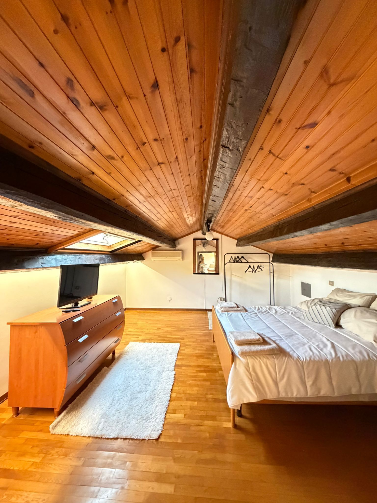 Una camera da letto con soffitto in legno, un letto, una cassettiera e una TV.