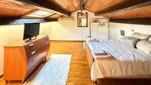 Een slaapkamer met houten plafond, een bed, een dressoir en een televisie.