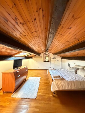 Un dormitorio con techo de madera, una cama, un aparador y un televisor.