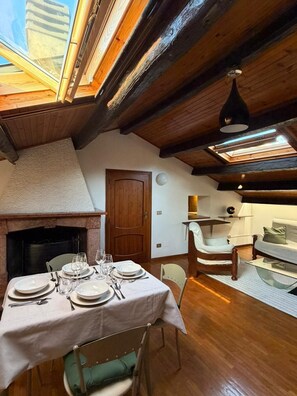 Un comedor con una mesa dispuesta para cuatro personas, una chimenea y una zona superior con un sofá y un sillón.