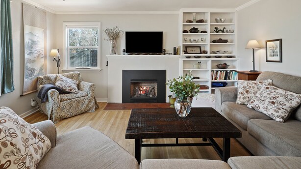 A living room with a fireplace, sofa, armchair, coffee table, and a TV. - NW Nest 30 Day Minimum (Bend)