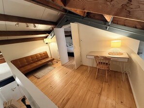 A loft-style bedroom with a wooden ceiling, a brown leather sofa, a desk with a lamp, and a bed in the background. - Stylish New York-Style Loft in Parnell  Spacious Auckland Escape with parking. (parnell)