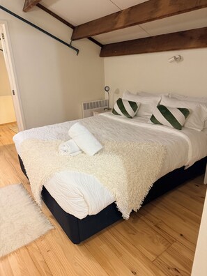 A neatly made bed with white bedding and green pillows, a bedside table with a lamp, and a wooden floor. - Stylish New York-Style Loft in Parnell  Spacious Auckland Escape with parking. (parnell)