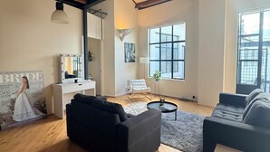 A spacious living room with wooden floors, a black sofa, a white chair, a small round table, and a large window. - Stylish New York-Style Loft in Parnell  Spacious Auckland Escape with parking. (parnell)