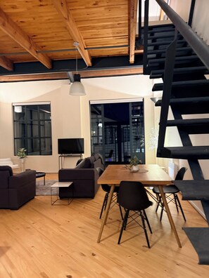 Ein modernes Interieur mit Holzbalkendecke, einer Essecke mit Tisch und Stühlen, einer Couch und einer Treppe.