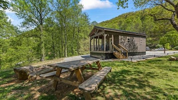 A cabin with a covered porch, a picnic table, and a view of a forested hill.