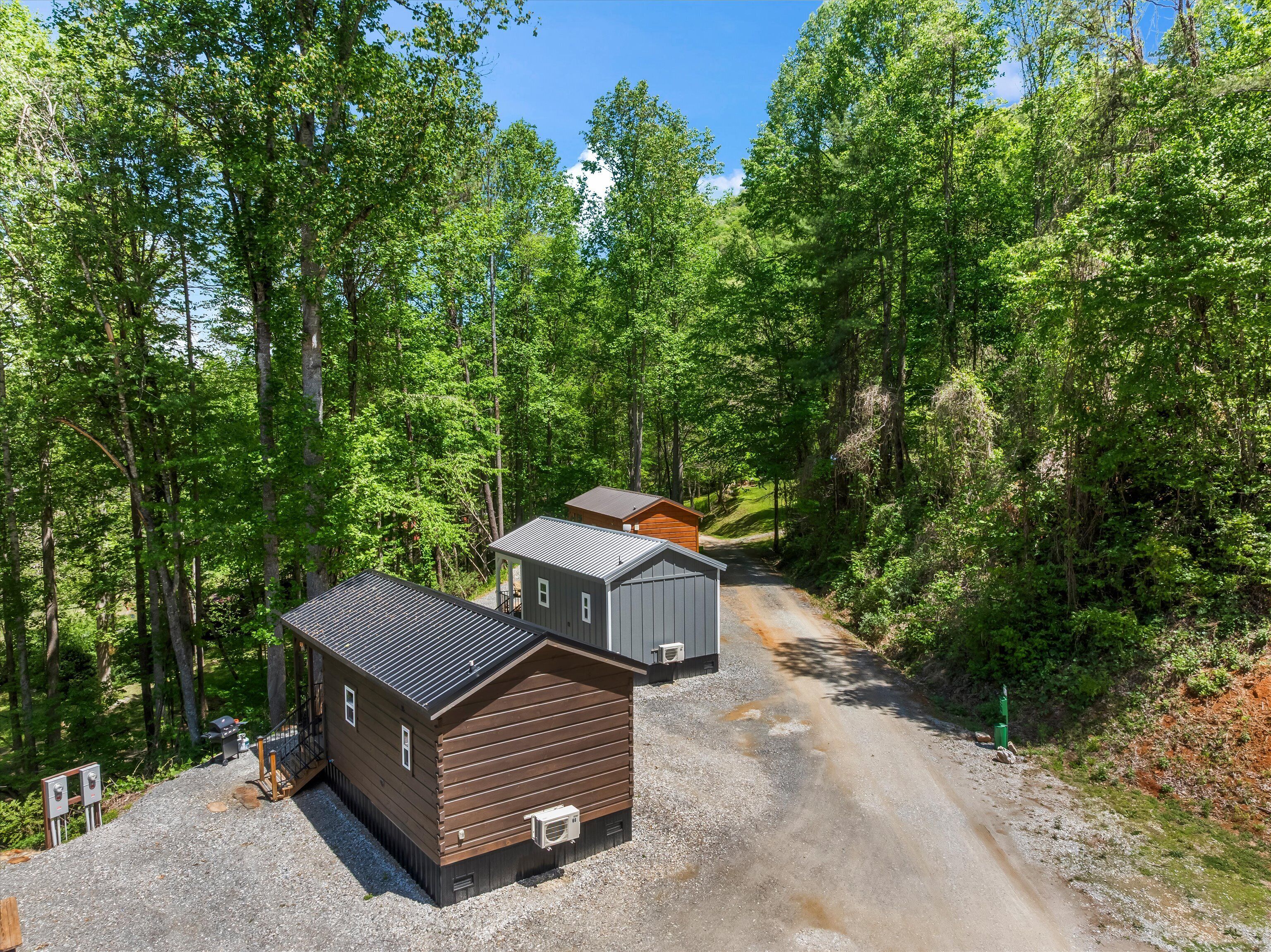 A cabin with a gravel driveway, surrounded by dense forest.