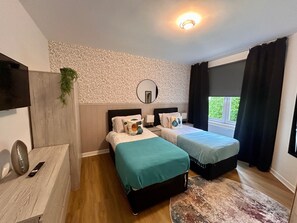 Camera da letto con due letti, uno specchio, una TV e una finestra con tende.