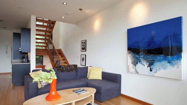 Een moderne woonkamer met een trap, een blauwe bank, een bijzettafeltje en een groot abstract schilderij.