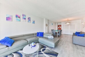 A living room with a grey sofa, a round coffee table, and a dining area with a table and chairs. - Ocean View 1-bedroom apartment with AC in beautiful Hollywood Beach pool, beach (Hollywood)