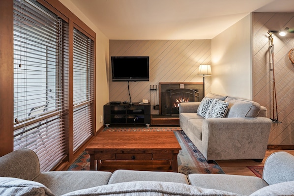 Ein Wohnzimmer mit einer Couch, einem Couchtisch, einem Kamin und einem Fernseher.