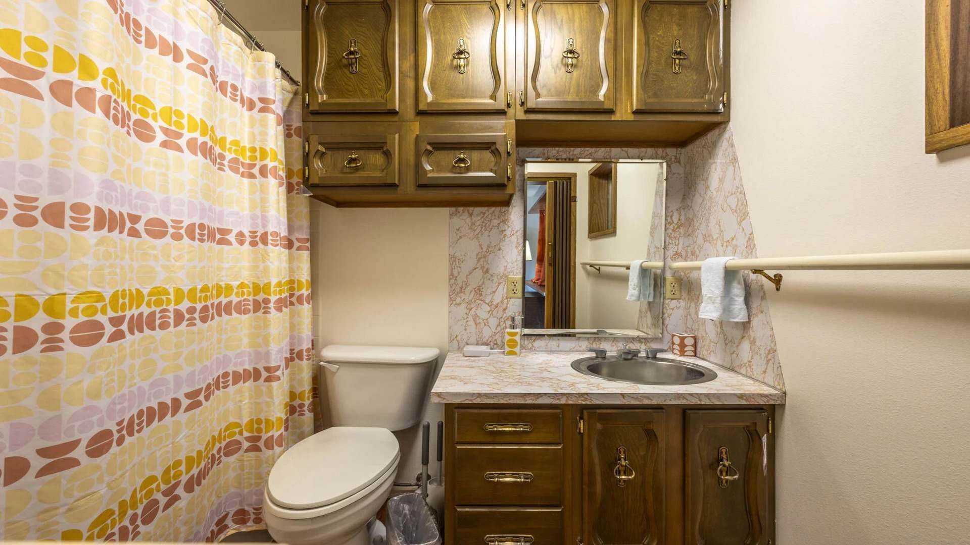 A bathroom with a toilet, sink, and wooden cabinets.