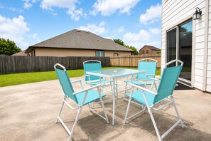 An outdoor patio with a table and chairs, a wooden fence, and a house in the background. - Spacious North Austin–Pflugerville Retreat - 6 King Beds - Modern Comfort (Pflugerville)