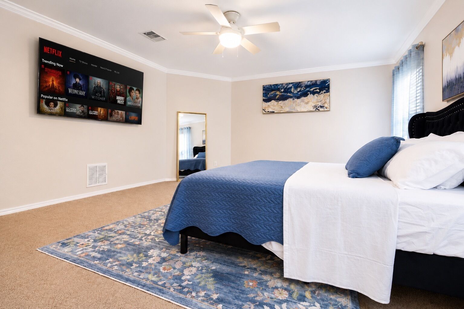 Ein Schlafzimmer mit einem Bett, einem Deckenventilator, einem an der Wand montierten Fernseher, der Netflix anzeigt, und einem Gemälde.