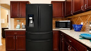 Een keuken met een zwarte Samsung koelkast, een magnetron, een blender en houten kastjes.