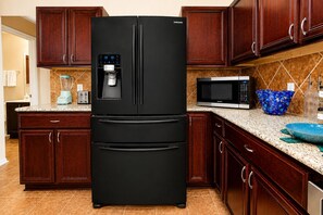 Una cocina con un refrigerador Samsung negro, un microondas, una licuadora y armarios de madera.