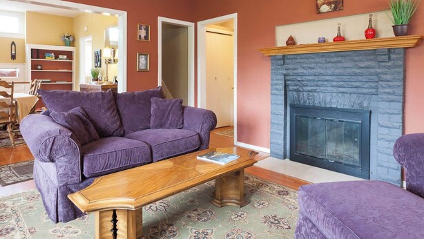 Ein Wohnzimmer mit einem violetten Sofa, einem Holztisch und einem Kamin.