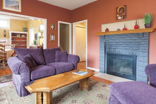 Ein Wohnzimmer mit einem violetten Sofa, einem Holztisch und einem Kamin.