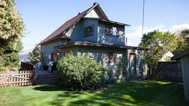 A two-story house with a sloped roof, a front porch, and a small front yard. - Heartbreak 30 day minimum (Hood River)