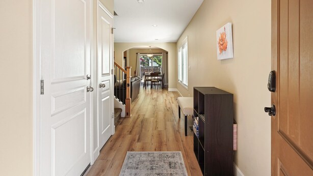 A hallway with a wooden floor, white doors, a staircase, a dining area, and a security keypad on a door. - Ellie 30 Days minimum (Bend)
