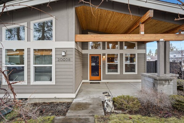 A modern two-story house with a grey exterior, large windows, and a wooden overhang. - Dwell 30 Day Minimum (Bend)