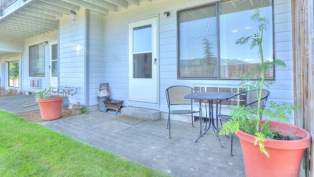 Une terrasse couverte avec une table et des chaises, une plante en pot et un petit espace aménagé en jardin.