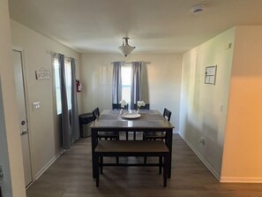 Et spiseområde med et bord, stole, en bænk, en loftslampe og en dør med et skilt.