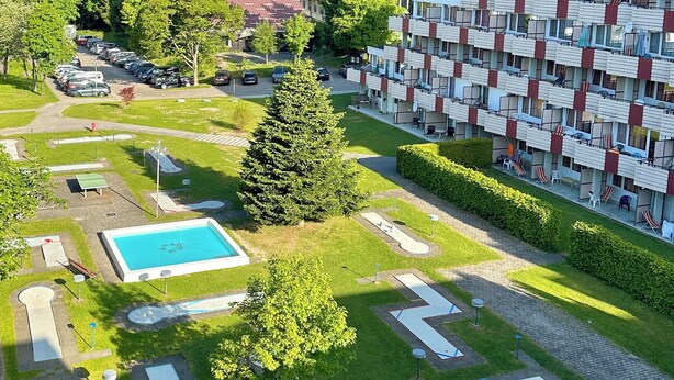 Un hôtel à plusieurs étages doté d’une piscine, de courts de tennis et bordé d’une forêt.