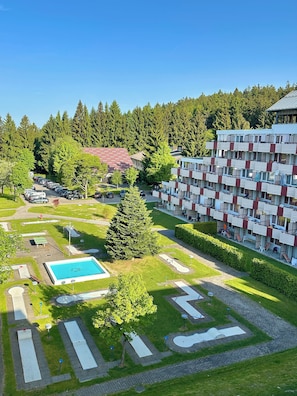 Un hôtel à plusieurs étages doté d’une piscine, de courts de tennis et bordé d’une forêt.