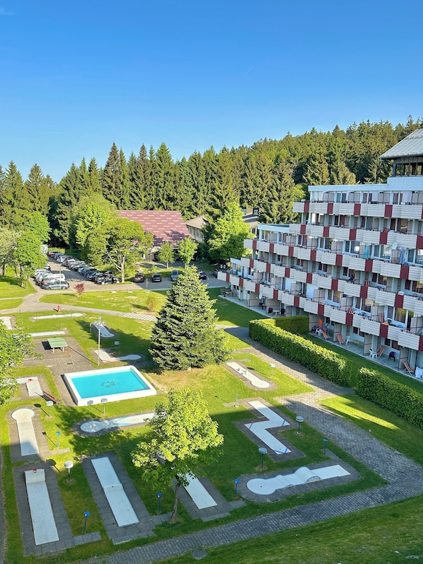 Ett hotell med flera våningar, en pool, tennisbanor och en skog som omger det.