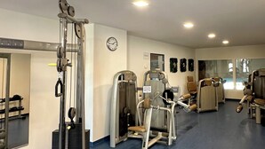 Une salle de sport équipée de machines d’exercice, avec une horloge et un miroir au mur.