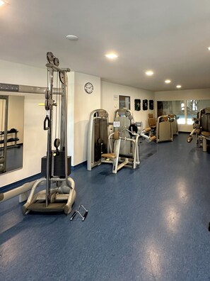 Ett gym med träningsmaskiner, en klocka och en spegel på väggen.