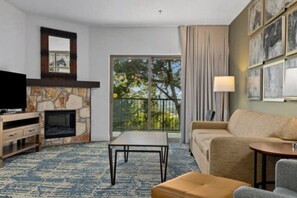 Ein Hotelzimmer mit Kamin, einer Sitzecke, einem Fernseher, einem kleinen Tisch und einem Balkon mit Blick auf Bäume.