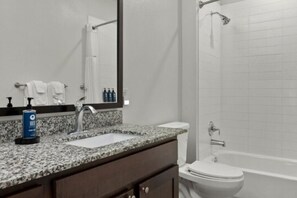 Ein Badezimmer mit Granitplatte, Waschbecken, Spiegel, Toilette und Badewanne.