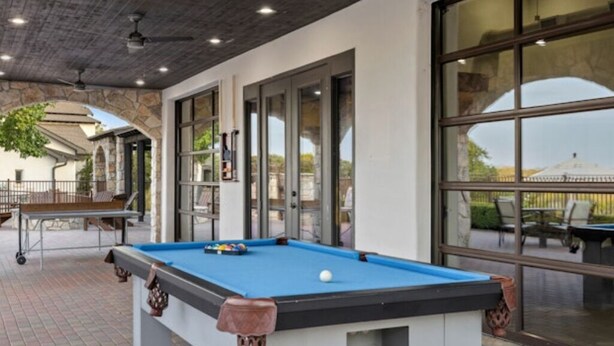 A pool table with a blue felt surface, a white wall with a stone archway, and a large window with a view of the outdoors. - BLOCK WM Stablewood Springs 1br (Ingram)