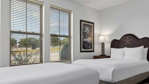A hotel room with two beds, a framed artwork on the wall, a bedside lamp, and a window with blinds. - BLOCK WM Stablewood Springs 1br (Ingram)