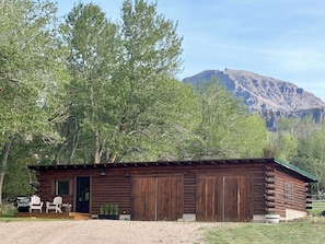 A rustic log cabin with a porch, two chairs, and a grill.