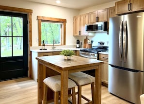A kitchen with wooden cabinets, a stainless steel refrigerator, a microwave, a stove, and a window with a view of trees.