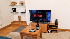 A living room with a television displaying Netflix, a bottle of wine, a plate with food, and a small table. - Pittoresquia Paris Gare de l'Est (Paris)