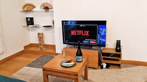 Ein Wohnzimmer mit Fernseher, der Netflix zeigt, einer Weinflasche, einem Teller mit Essen und einem kleinen Tisch.