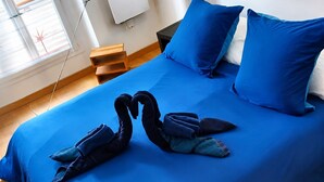 A bed with a blue bedspread, two pillows, and a pair of folded towels arranged in a swan shape. - Pittoresquia Paris Gare de l'Est (Paris)