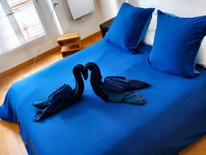 Ein Bett mit blauer Bettdecke, zwei Kissen und ein Paar Handtücher, die als Schwan drapiert sind.