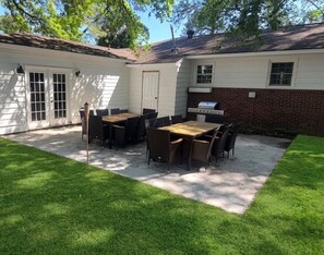 Un jardin avec une table et des chaises de patio, un barbecue et une porte donnant accès à un garage.