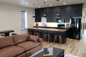 A modern kitchen with dark cabinets, a wooden island, bar stools, and a brown leather sofa. - Bird's Eye View of Stanton (Stanton)